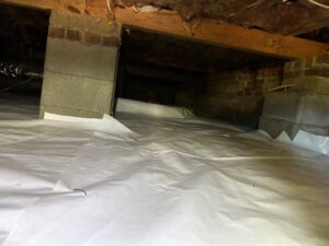 White vapor barrier covering a crawl space floor around brick and block piers