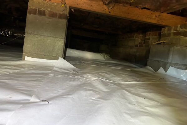 White vapor barrier covering a crawl space floor around brick and block piers
