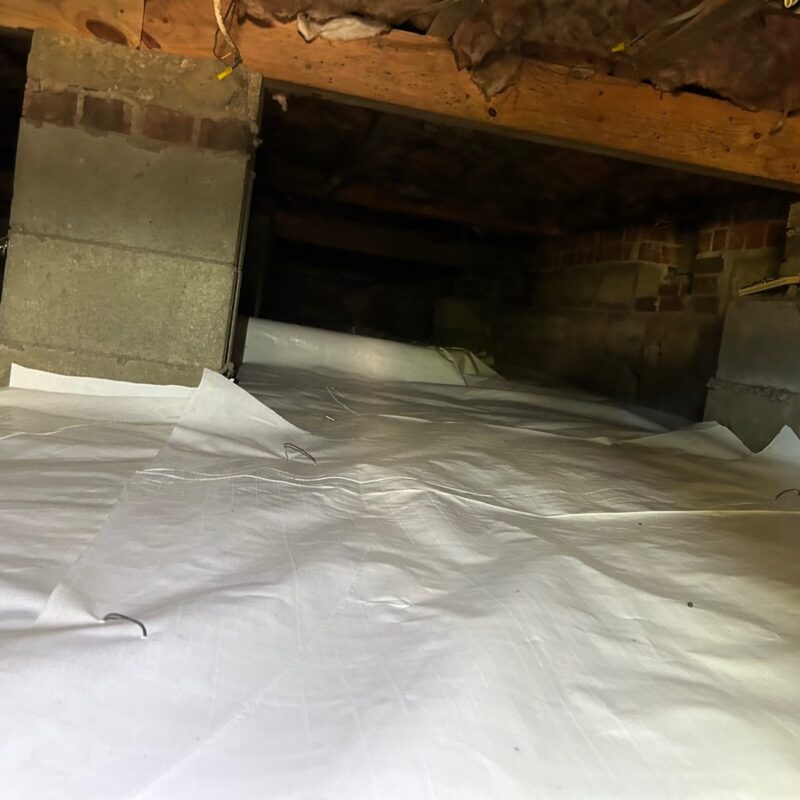 White vapor barrier covering a crawl space floor around brick and block piers