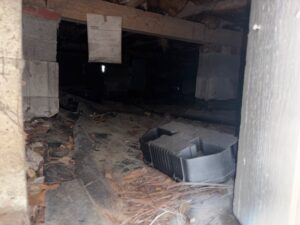 Apartment crawl space with bare dirt, debris and an old duct before the vapor barrier was installed