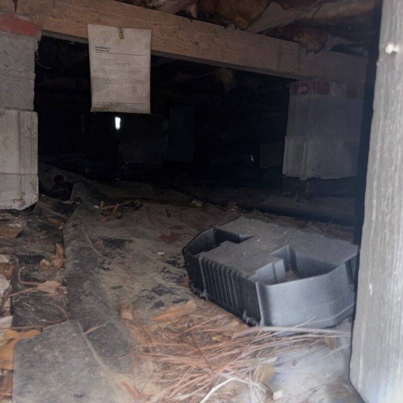 Apartment crawl space with bare dirt, debris and an old duct before the vapor barrier was installed