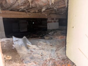 Crawl space with block piers and debris on dirt before vapor barrier installation