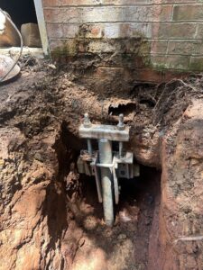 Galvanized helical pile bracket attached below a brick foundation wall in red clay soil